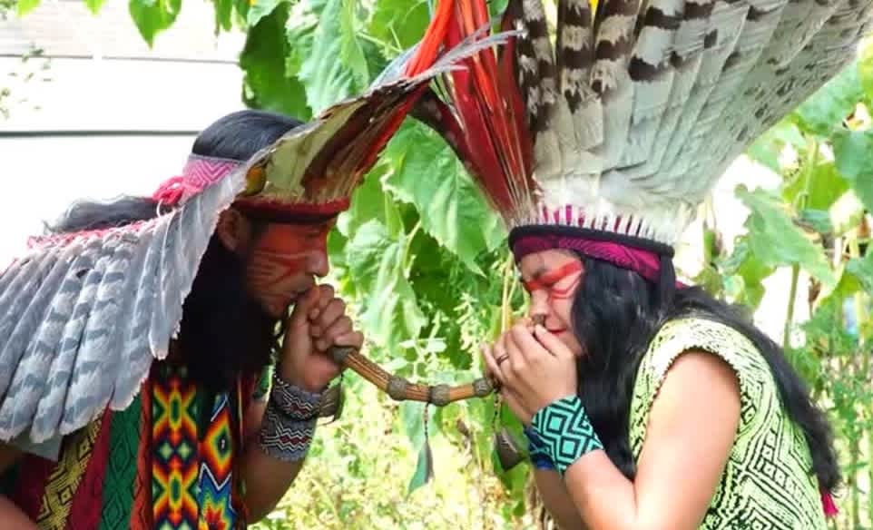 Blowing Rapé with Tepi two Indigenous people from tribe Indians with traditional feather headdress